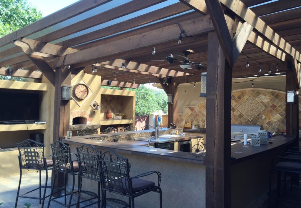 A Newly Renovated Patio including Outdoor Kitchen with grille, sink, refrigerator, countertops and wooden pergola - CK Contracting - Home Outdoor Renovations - Mount Pleasant, SC