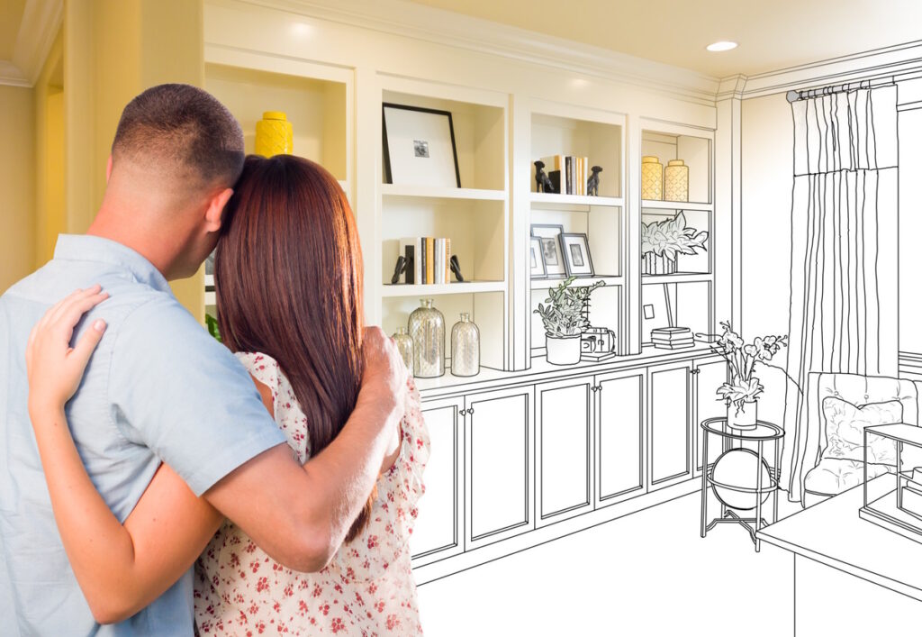 A couple are looking at draft drawings of their home office. with a bookshelf on the back wall with storage on the bottom of the wall, a desk with a chair, and windows on the right of the room, CK Contracting, home remodeling Charleston S.C.