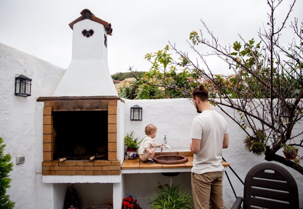 A male is standing in front of the outdoor brick kitchen with a little boy sitting at the sink, The Pros and Cons of a Brick Outdoor Kitchen, CK Contracting, Home Renovations, Mt. Pleasant, SC.